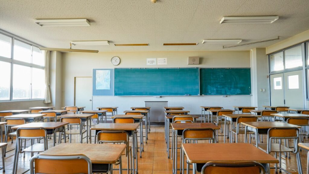 学校の教室、後方から黒板の方向を向いている。人は誰もいない。